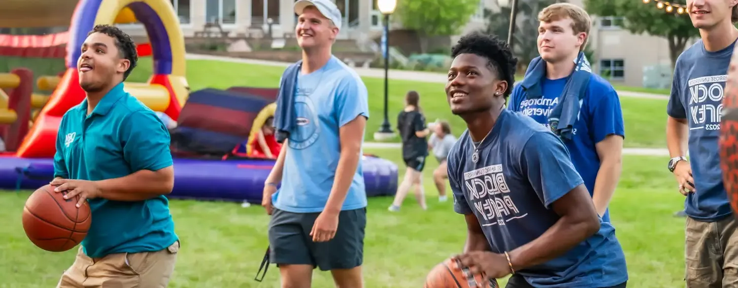 Two students shooting basketballs outside at an evening event